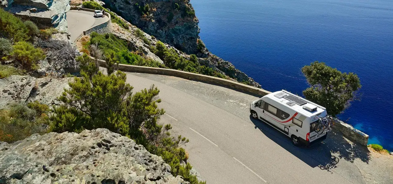 Camping-car sur une route c&ocirc;ti&egrave;re corse, id&eacute;al pour calculer le prix ferry corse pour camping car. Mer bleue et falaises.