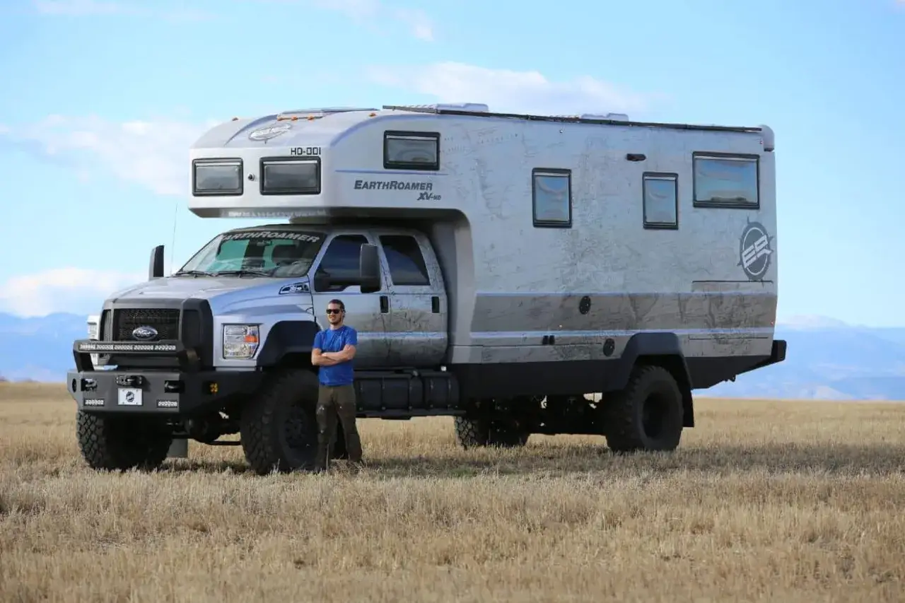 Un homme pose devant un camping-car tout-terrain EarthRoamer XV-HD argenté, prêt pour l'aventure.