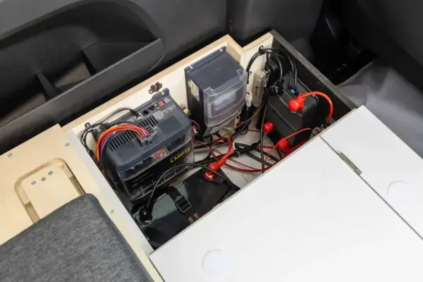 Système de batteries et de câblage pour un chauffage pour van sans électricité. L'installation est bien rangée dans un compartiment en bois.