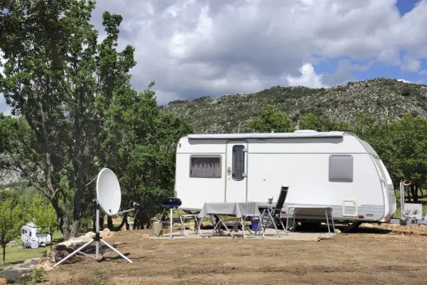 Schéma installation TV camping-car : parabole satellite devant une caravane, avec table et chaises dressées pour un repas en plein air.